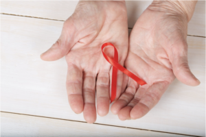 Hands of an older woman holding a red silk ribbon for World AIDS Day, 12/1.